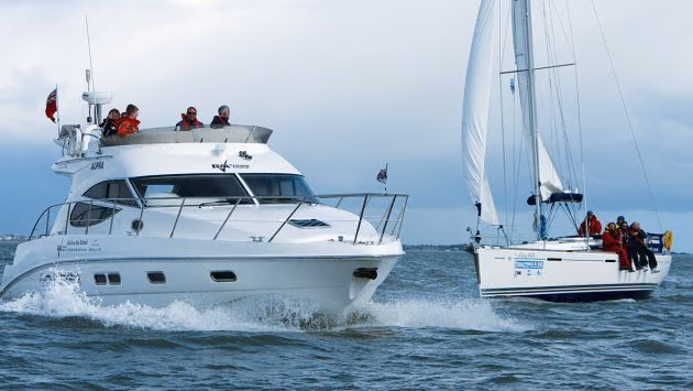A motor yacht and a sailing yacht with crews in sailing jackets at sea