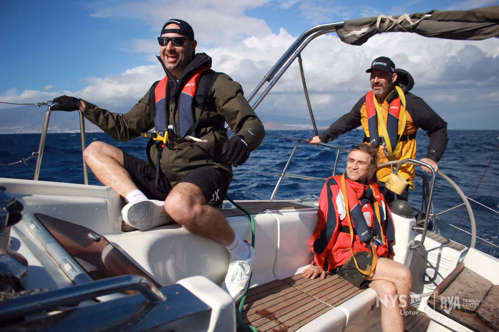 Crew in lifejackets in the cockpit of a yacht under way at sea